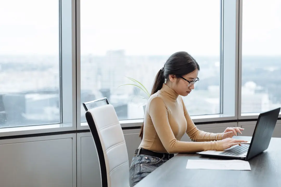 Woman working on a laptop in a bright, modern office with a view